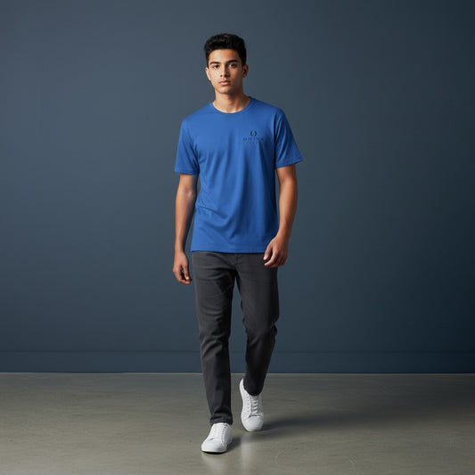 Young man wearing a blue Omina performance tee with Future Self Proud branding, paired with grey jeans and sneakers.
