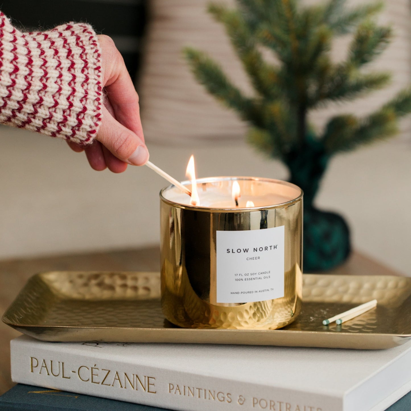 Slow North Cheer Signature 3-Wick Candle with seasonal festive label and three burning wicks on a decorative surface.