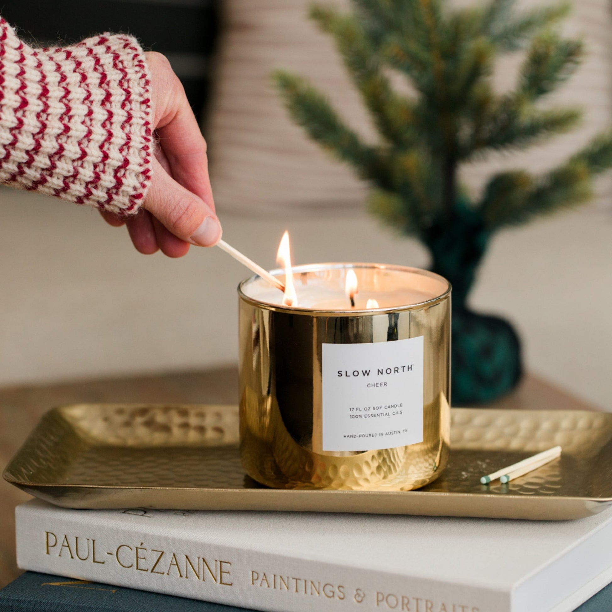 Slow North Cheer Signature 3-Wick Candle with seasonal festive label and three burning wicks on a decorative surface.