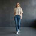 Omina beige heavyweight cotton boxy t-shirt with raw edge detail and subtle logo, worn by a woman with hands in pockets.