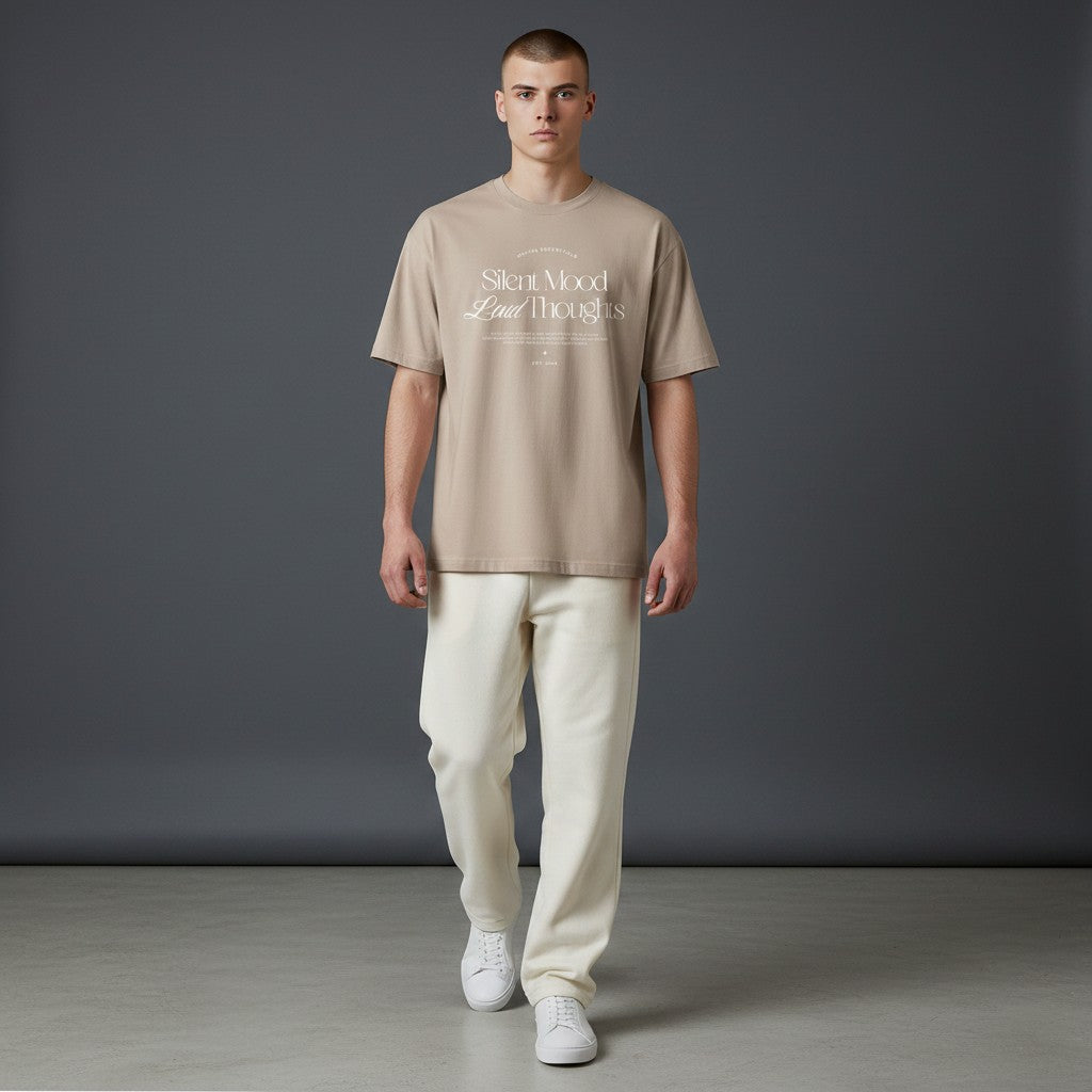 Male model wearing an Omina beige cotton jersey tee with Silent Mood graphic text, paired with cream trousers.