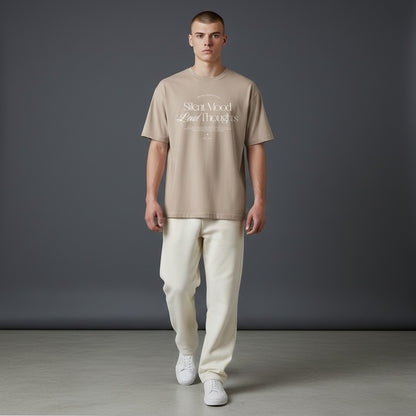 Male model wearing an Omina beige cotton jersey tee with Silent Mood graphic text, paired with cream trousers.