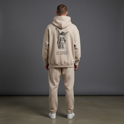 Back view of a man wearing an Omina beige oversized fleeced hoodie with an angel graphic and text print.