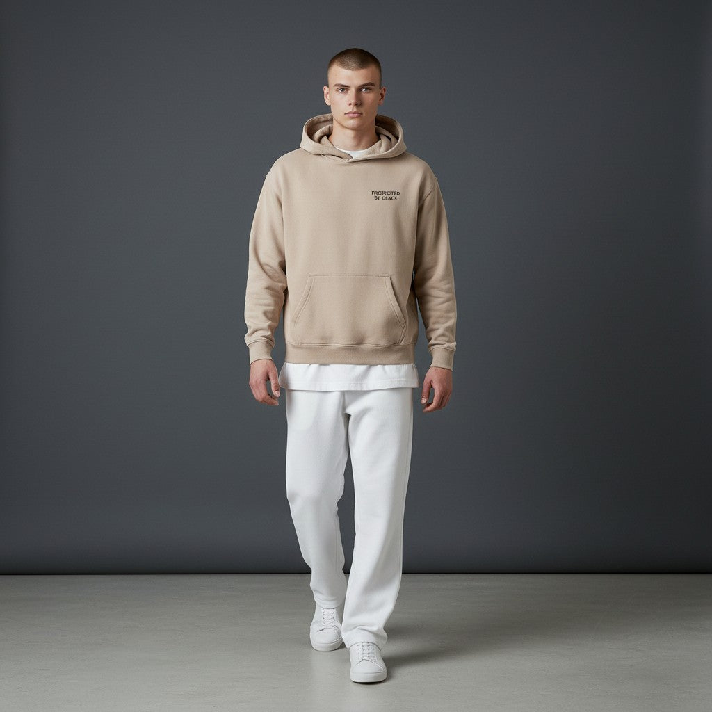 Model wearing an Omina beige oversized fleeced hoodie with Protected By Grace text, paired with white trousers.
