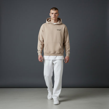 Model wearing an Omina beige oversized fleeced hoodie with Protected By Grace text, paired with white trousers.