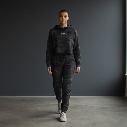 Model wearing Omina Essentials black camo print cropped hoodie and matching joggers in a minimalist studio setting.