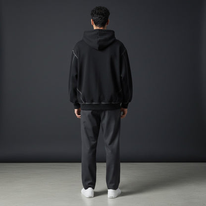 Back view of a man wearing an Omina black boxy fleece zip hoodie with white contrast stitching and drop shoulders.