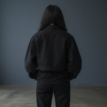 Back view of a woman wearing an Omina black cropped denim jacket with structured collar and long sleeves.