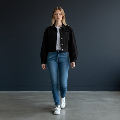 A model wearing an Omina black cropped denim jacket with a button-front closure over a white t-shirt and blue jeans.