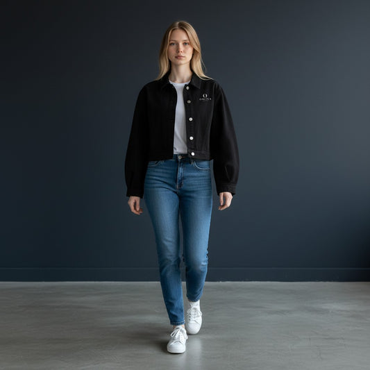 A model wearing an Omina black cropped denim jacket with a button-front closure over a white t-shirt and blue jeans.