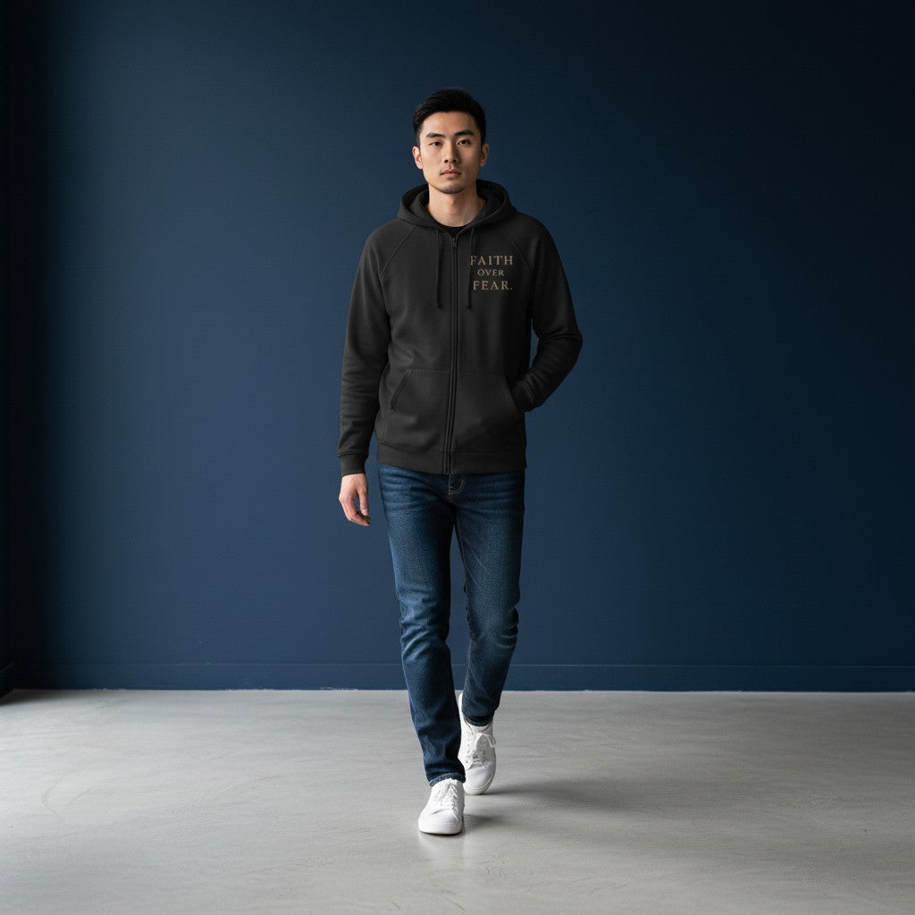 A man wearing an Omina black heavyweight cotton zip hoodie with Faith Over Fear text, paired with jeans and sneakers.