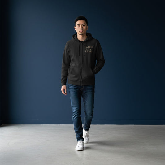 A man wearing an Omina black heavyweight cotton zip hoodie with Faith Over Fear text, paired with jeans and sneakers.