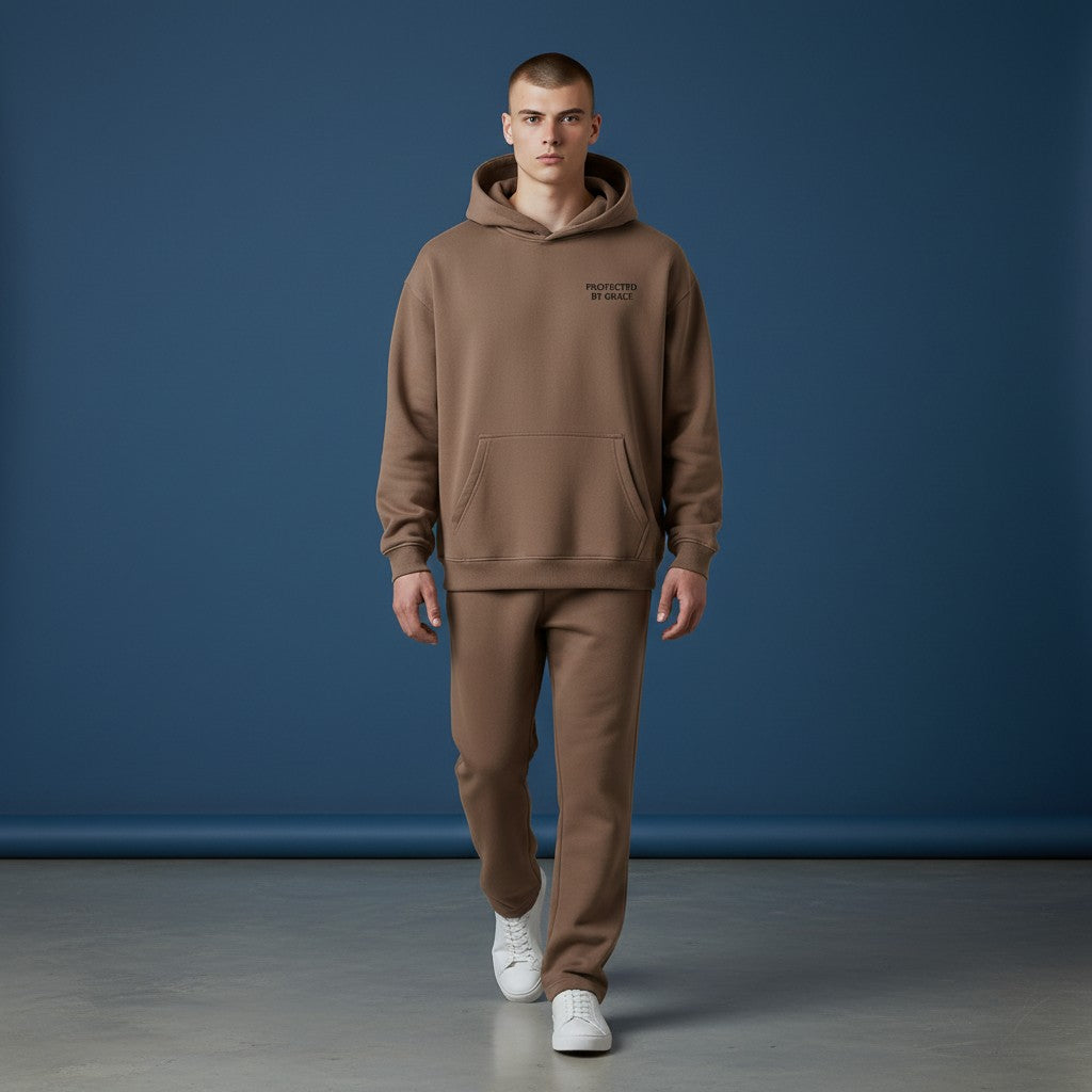 Male model wearing an Omina brown oversized fleeced hoodie with Protected By Grace text and matching sweatpants.