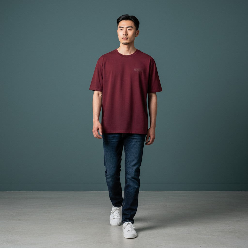 Omina burgundy cotton t-shirt with minimalist logo detail on chest, worn by a man with dark jeans and white sneakers.