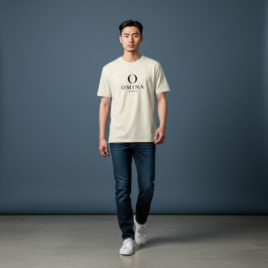A man wearing an Omina cream-colored cotton crew neck T-shirt with a black O mascot logo, styled with dark blue jeans.