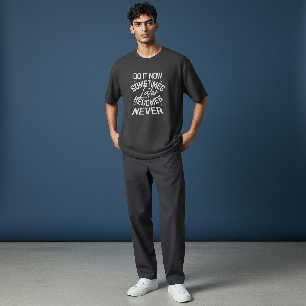 Man wearing a charcoal Omina cotton t-shirt with Do It Now graphic text, styled with dark trousers and white sneakers.