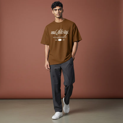 Omina Essentials oversized brown heavyweight cotton t-shirt with white "Own Your Story" graphic print and ESTD 2026 detail.