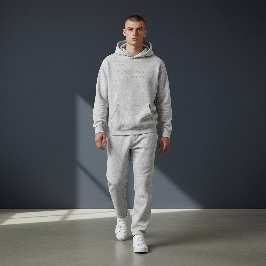 Omina Essentials light grey fleeced boxy hoodie with gold logo on chest. Relaxed fit with drop shoulders and ribbed cuffs.