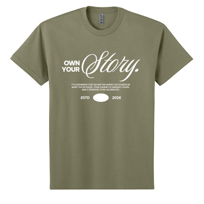Omina Essentials olive green heavyweight cotton t-shirt with "Own Your Story" graphic print and ESTD 2026 detail.