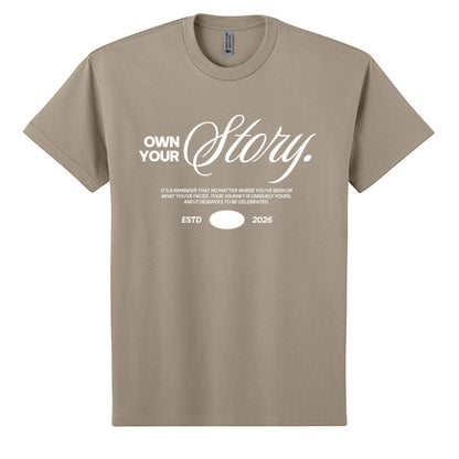Omina Essentials tan heavyweight cotton t-shirt with white "Own Your Story" graphic and ESTD 2026 detail.