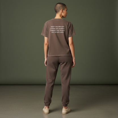 OMINA Essentials brown cotton t-shirt with vintage wash and white text reading "TRUST THE PROCESS. HONOR THE JOURNEY. EMBRACE THE WOMAN YOU ARE BECOMING."