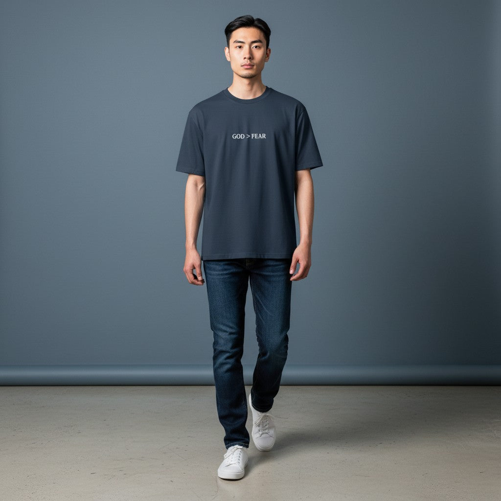 Model wearing Omina heavyweight cotton t-shirt in charcoal with God > Fear graphic print, paired with blue jeans.