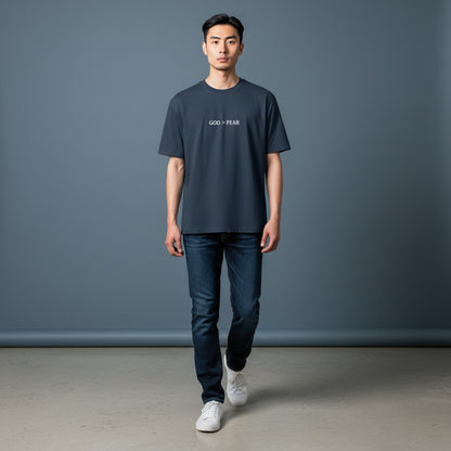 Model wearing Omina heavyweight cotton t-shirt in charcoal with God > Fear graphic print, paired with blue jeans.