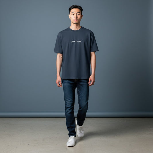 Model wearing Omina heavyweight cotton t-shirt in charcoal with God > Fear graphic print, paired with blue jeans.