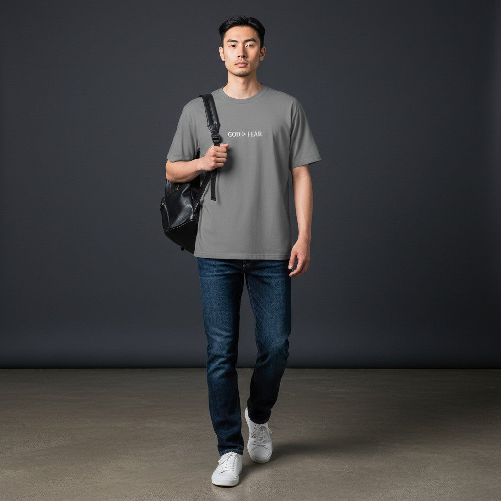 Model wearing Omina grey heavyweight cotton crew neck t-shirt with God > Fear graphic, paired with jeans and backpack.