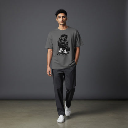 A man wearing a grey Omina O Urban T-Shirt with a graphic print, paired with dark trousers and white sneakers.