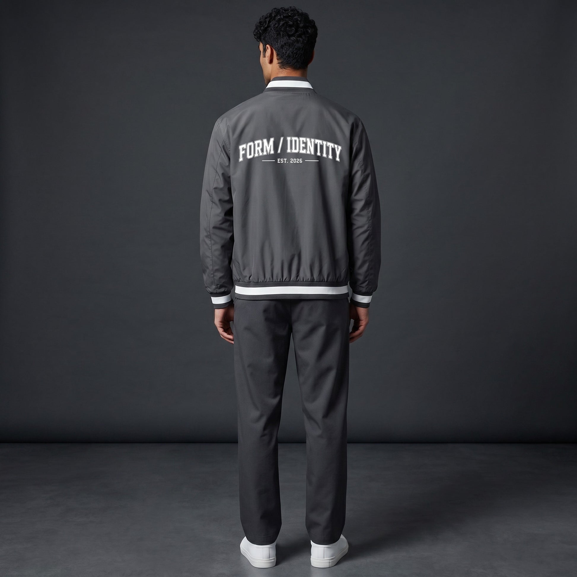 Omina grey insulated varsity jacket with white "FORM / IDENTITY EST. 2026" graphic on back and striped rib-knit collar, cuffs, and hem.