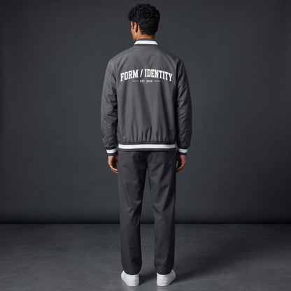 Omina grey insulated varsity jacket with white "FORM / IDENTITY EST. 2026" graphic on back and striped rib-knit collar, cuffs, and hem.
