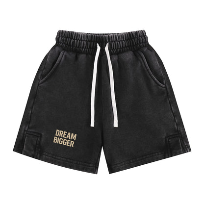 Omina Kids black snow-washed shorts with elastic waistband, white drawstring, and "DREAM BIGGER" graphic.