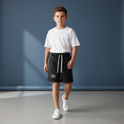 Omina Kids snow-washed black shorts with elastic waistband, white drawstring, and "DREAM BIGGER" graphic.