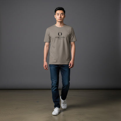 A man wearing an Omina Meet O T-shirt in taupe cotton with a black mascot graphic, paired with dark blue jeans.