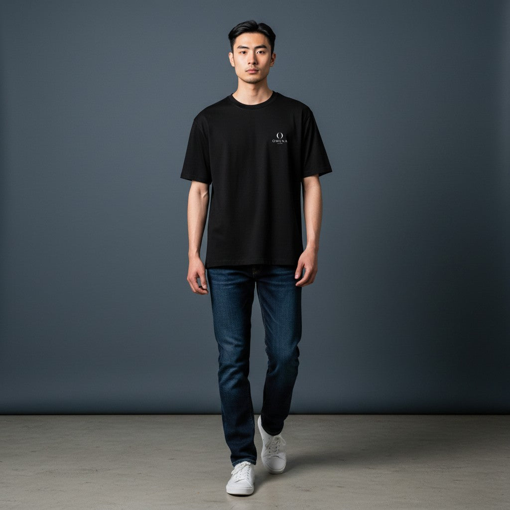 Model wearing an Omina minimalist black ring-spun cotton t-shirt with a small chest emblem and dark blue jeans.