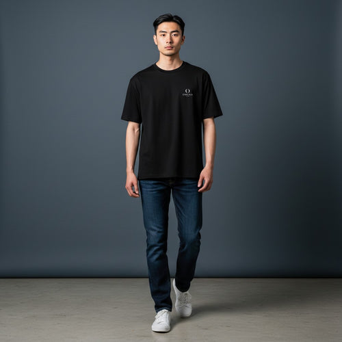 Model wearing an Omina minimalist black ring-spun cotton t-shirt with a small chest emblem and dark blue jeans.