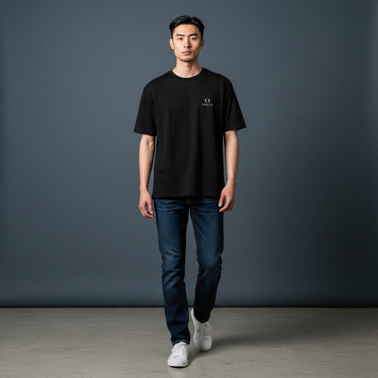 Model wearing an Omina minimalist black ring-spun cotton t-shirt with a small chest emblem and dark blue jeans.