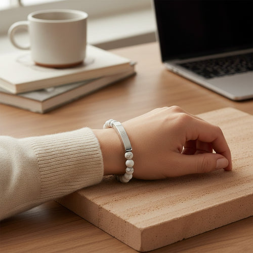 Omina natural stone stretch bracelet with white marbled beads and a polished stainless steel engraved bar on a wrist.