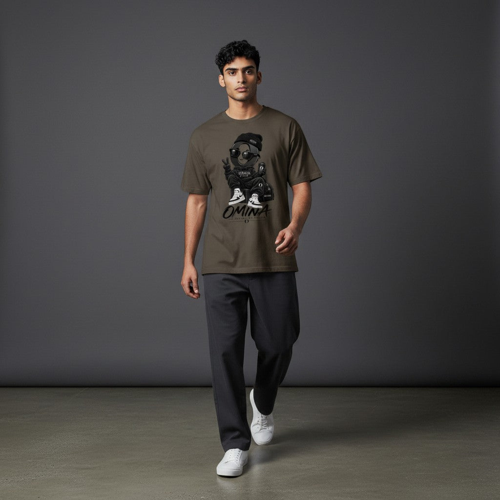 Model wearing an Omina olive green cotton t-shirt with a graphic print of a character in sunglasses and a beanie.