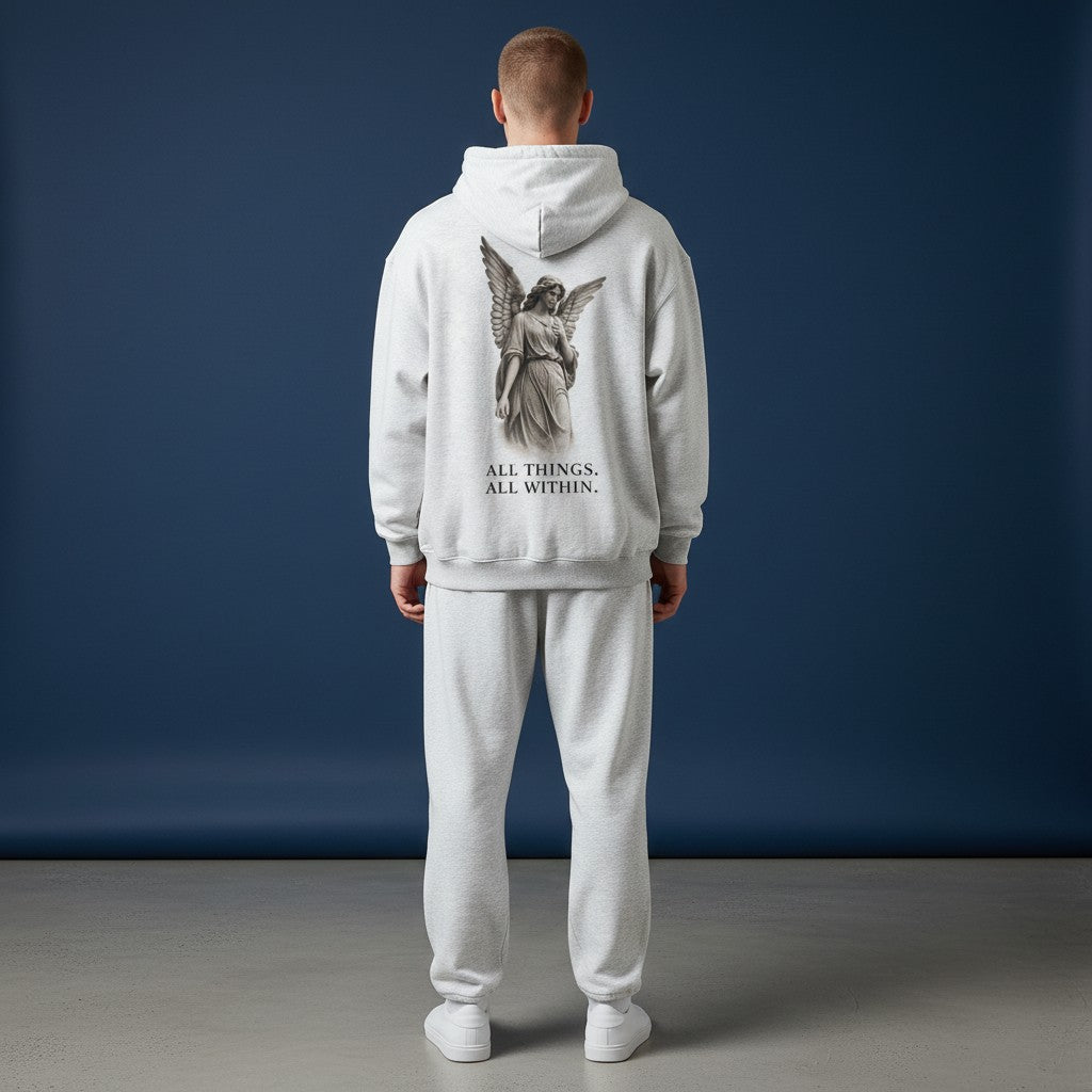 Omina oversized grey fleeced hoodie with angel graphic and text on back worn by a man against a blue background