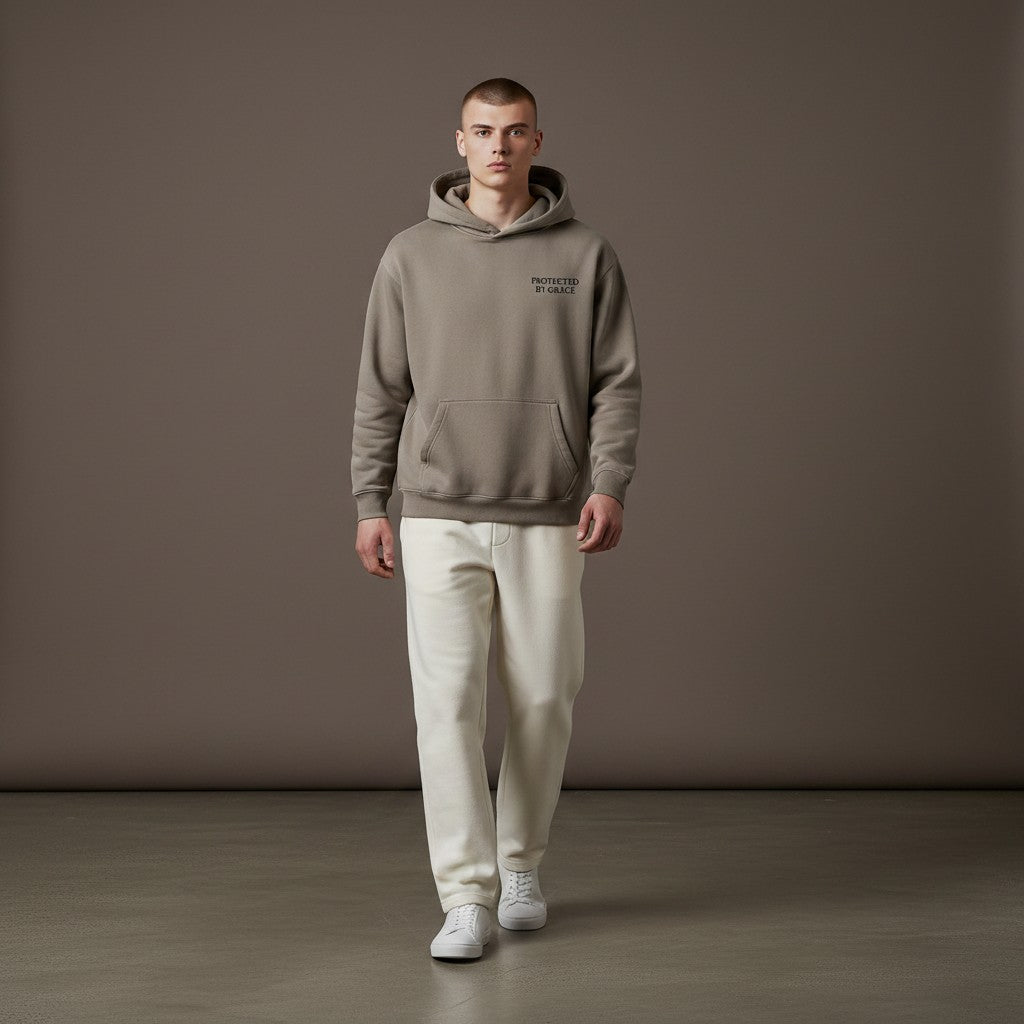 Omina oversized taupe fleeced hoodie with Protected By Grace text, worn by a man with cream trousers and white sneakers.