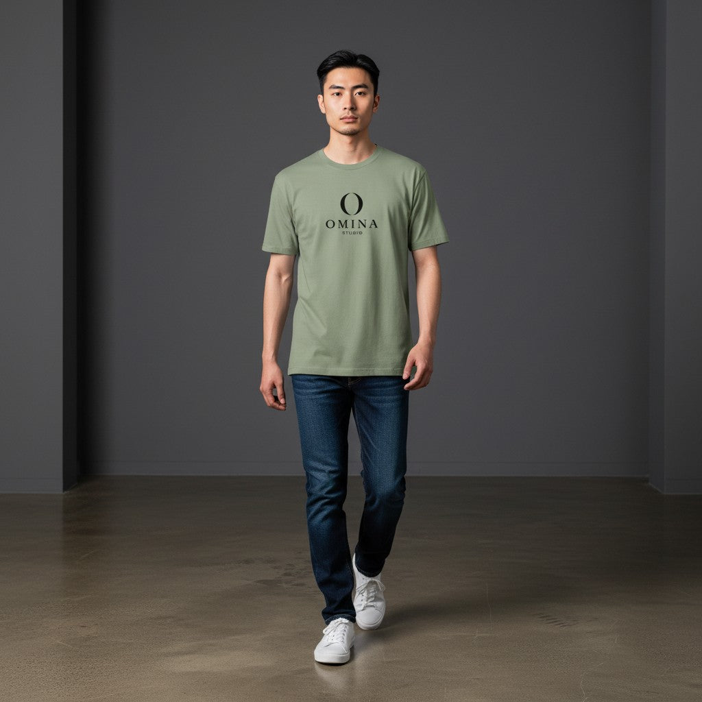 A man wearing an Omina sage green cotton crew neck t-shirt with a black Omina Studio mascot graphic, paired with jeans.