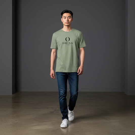 A man wearing an Omina sage green cotton crew neck t-shirt with a black Omina Studio mascot graphic, paired with jeans.