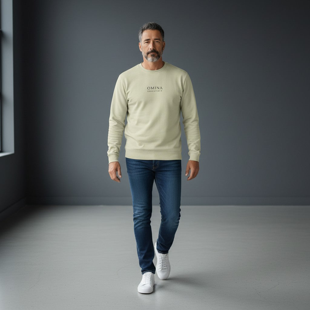 A man wearing a sage green Omina long sleeve crew neck shirt with drop shoulders, styled with blue jeans and sneakers.