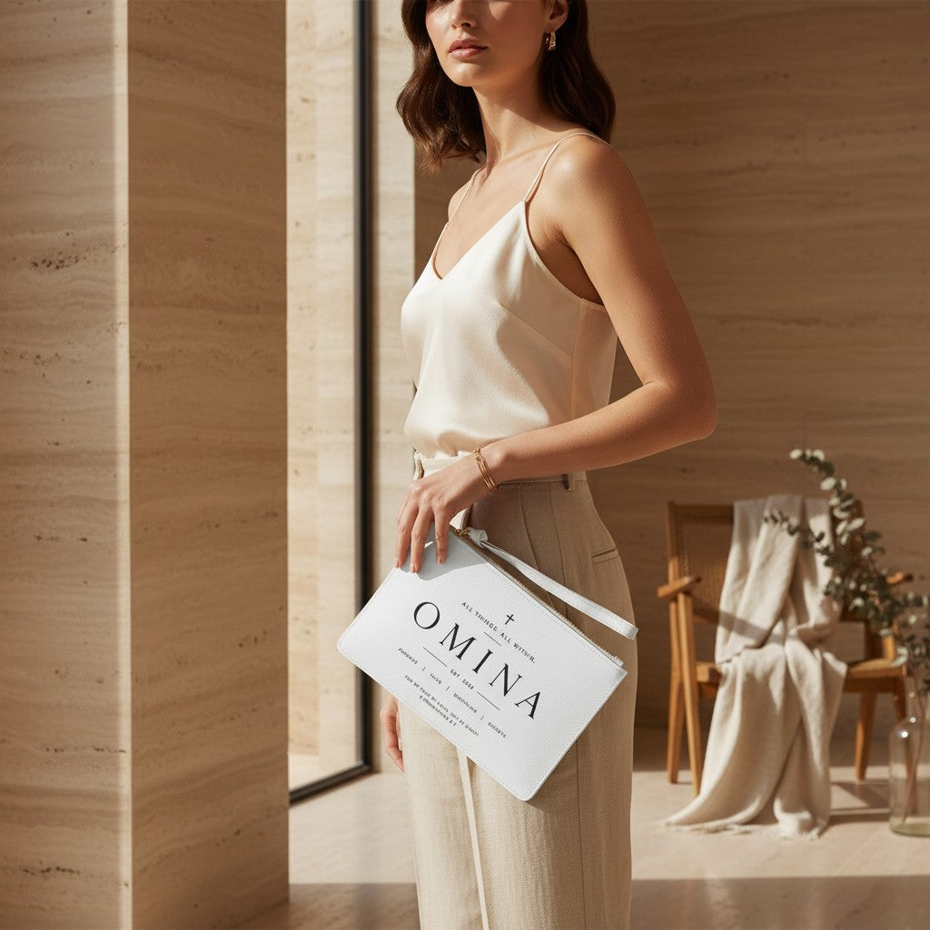 Woman holding a white Omina saffiano PU leather wristlet clutch with typographic scripture design and gold zipper.