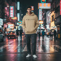 Omina Studio beige hooded sweatshirt with kangaroo pocket and black logo on chest. Made from midweight cotton-poly blend.