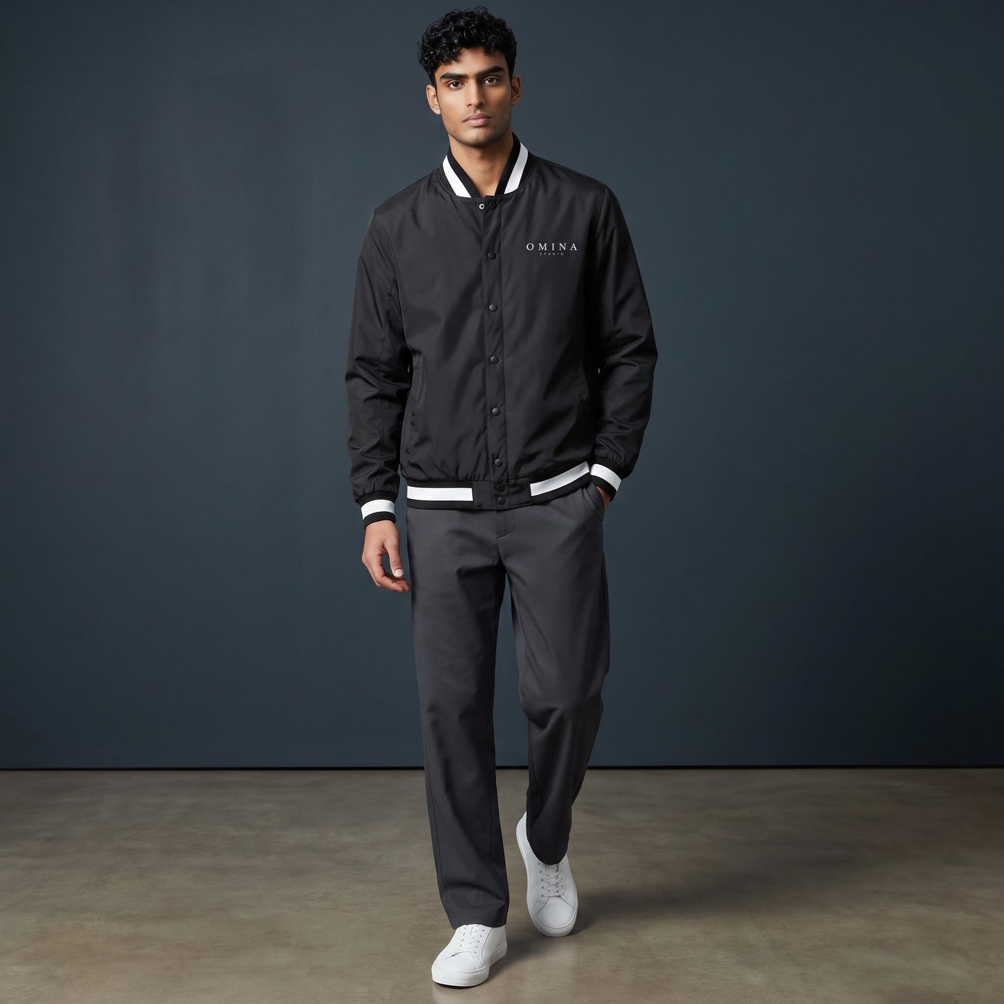 OMINA Studio black insulated varsity jacket with white striped collar, cuffs, and hem. Water-resistant.