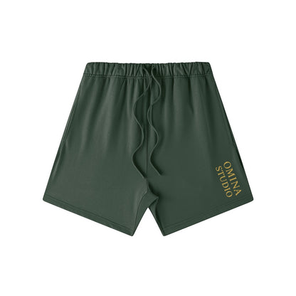 Omina Studio heavyweight dark green cotton French terry shorts with drawstring and gold logo.
