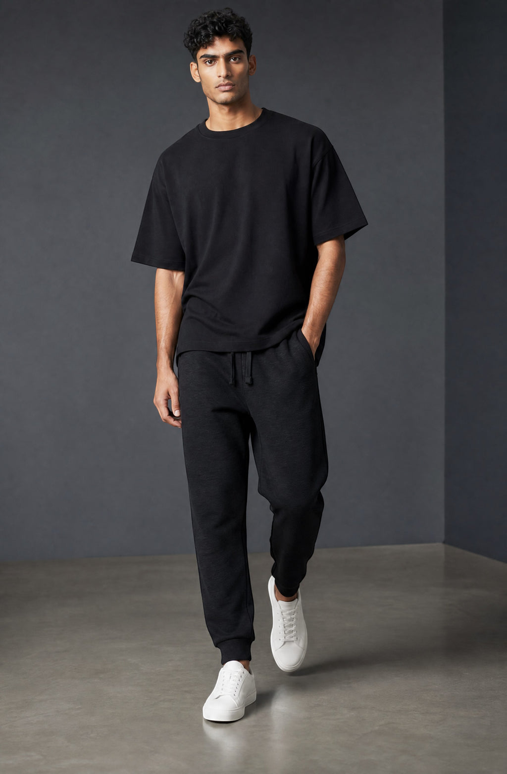 OMINA Studio black premium fleece joggers with tapered fit, ribbed cuffs, and flat drawcords. Model is wearing white sneakers.